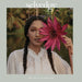 Woman holding a large pink flower with a tropical background, featuring the brand 'selvedge'.