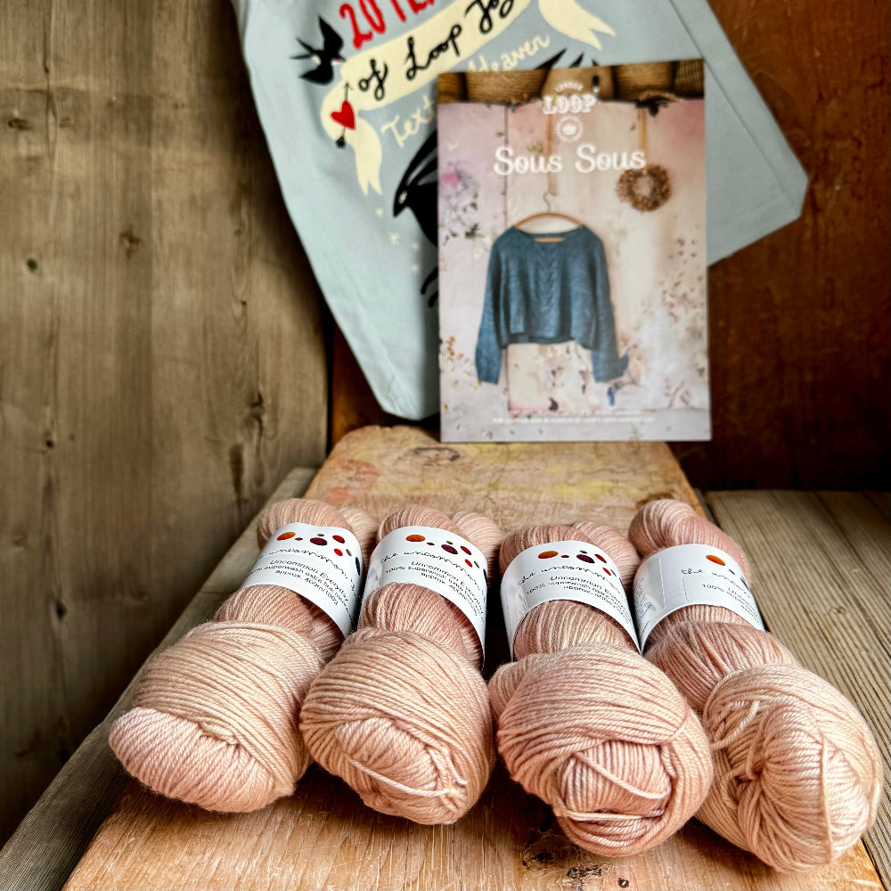 Four skeins of pink yarn on a wooden surface with a patterned card in the background.