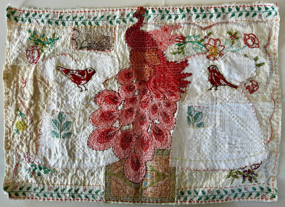 Textile art piece with floral and bird designs on a white background