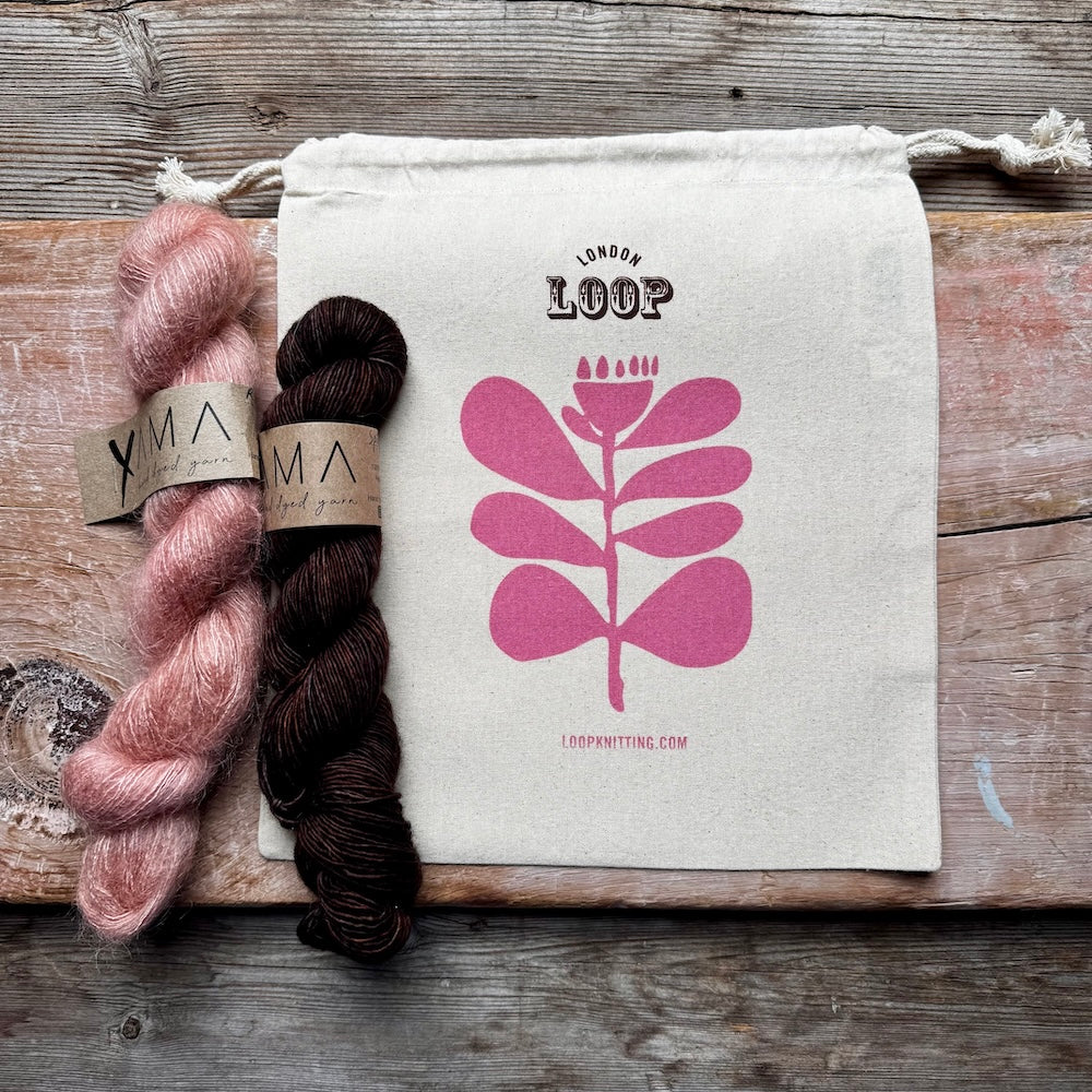 Two skeins of yarn and a white drawstring bag with pink floral design on a wooden surface.