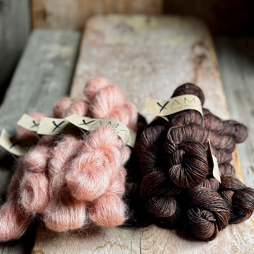 Two skeins of yarn, one pink and one brown, on a wooden surface with 'YAMA' labels.