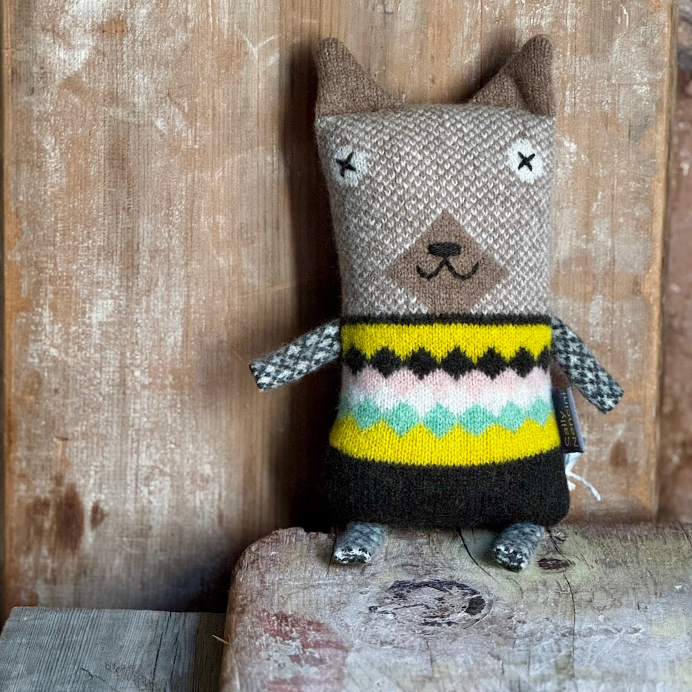 Knitted toy dog wearing a colorful sweater on a wooden surface