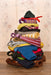 A stack of colorful handmade knit baby socks and booties arranged in a pyramid shape on a wooden surface, with a soft floral wallpaper background.