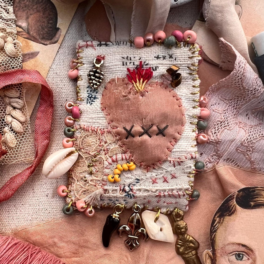 Textile art piece with beads and fabric on a textured surface