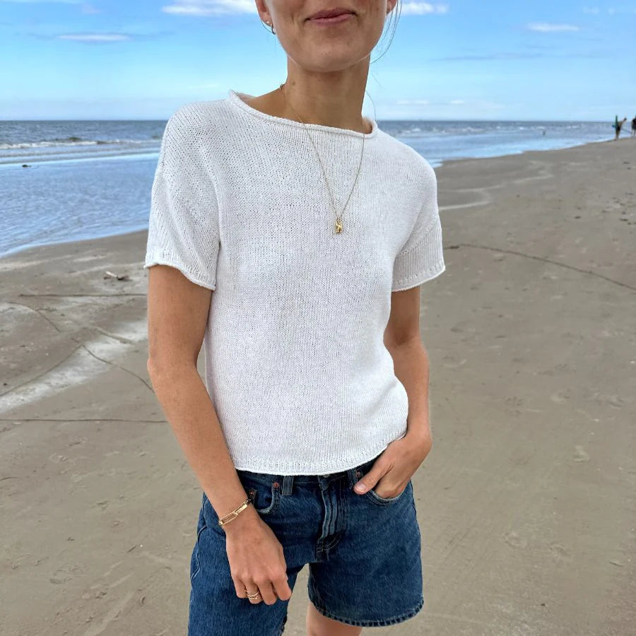 Person wearing a white shirt and blue shorts standing on a beach.