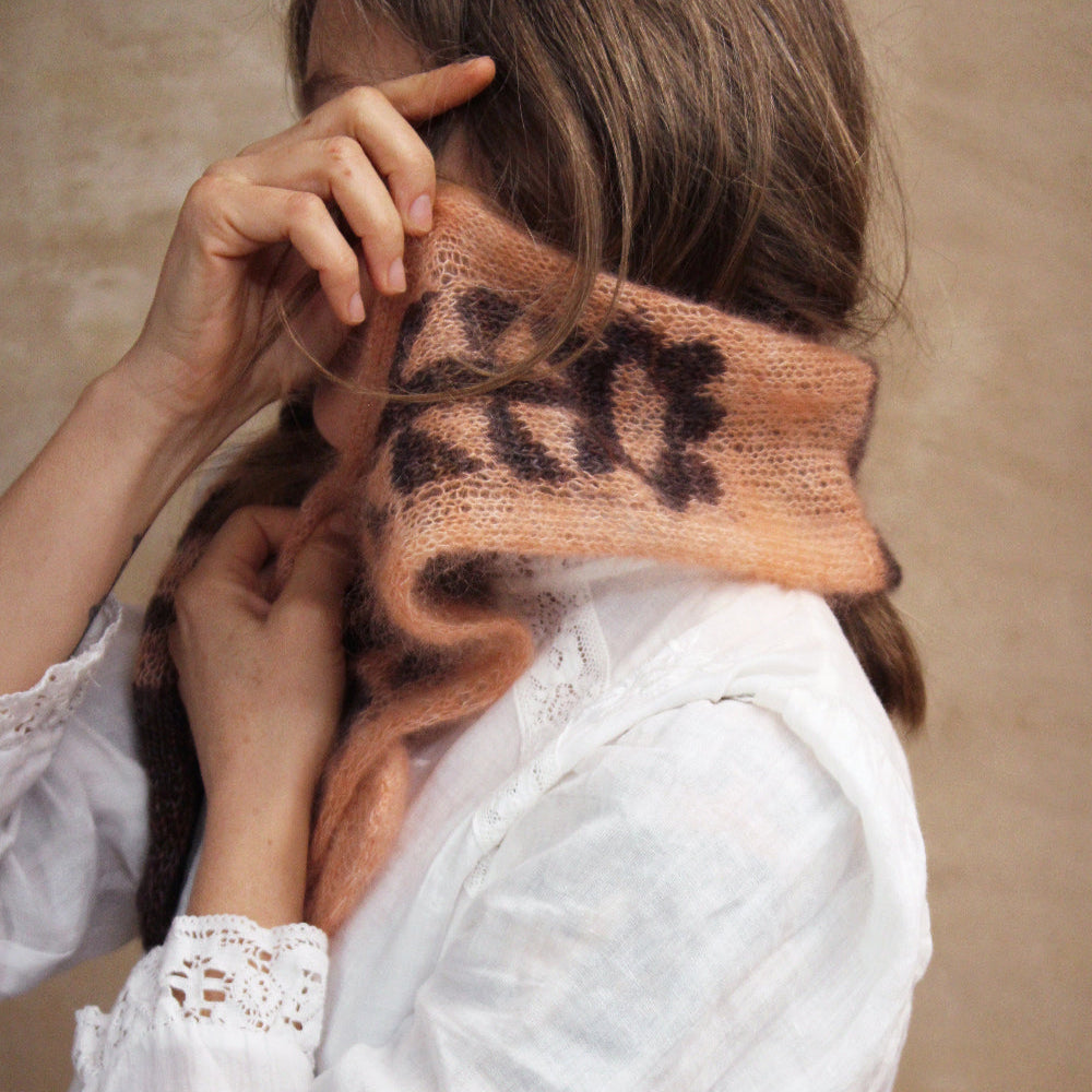 Person wearing a white shirt with a brown knitted sleeve covering part of their face.