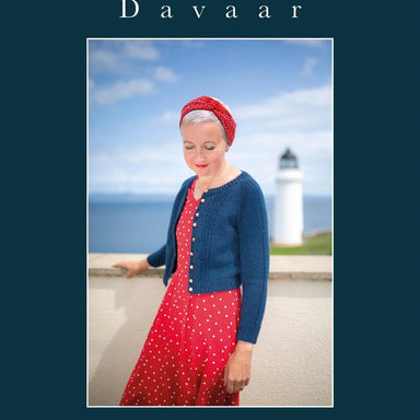 Woman in a blue cardigan and red dress standing in front of a lighthouse with 'Davaar' branding.