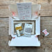 A Sashiko stitch embroidery kit in a white cardboard box with a window showing thread spools inside, placed on a wooden surface. A red thread spool tag hangs to the right with the text 'SASHIKOSTITCH HORIZOWA NAMI'.