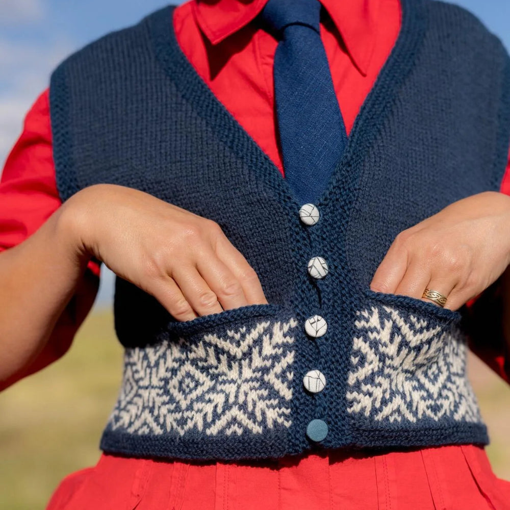 Person wearing a navy knitted vest with a patterned design over a red shirt and tie.