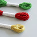 Three skeins of thread in green, red, and yellow on a light gray background