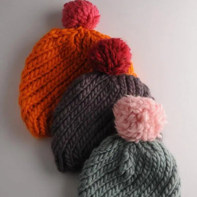Three knitted hats with colorful pom-poms on a light gray background