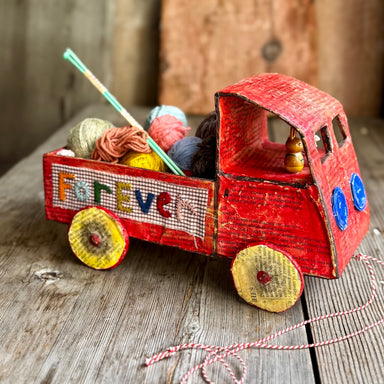 Red toy truck with yarn and knitting needles on a wooden surface