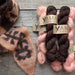 Three skeins of yarn in pink, brown, and black with 'YAMA' labels on a wooden surface.
